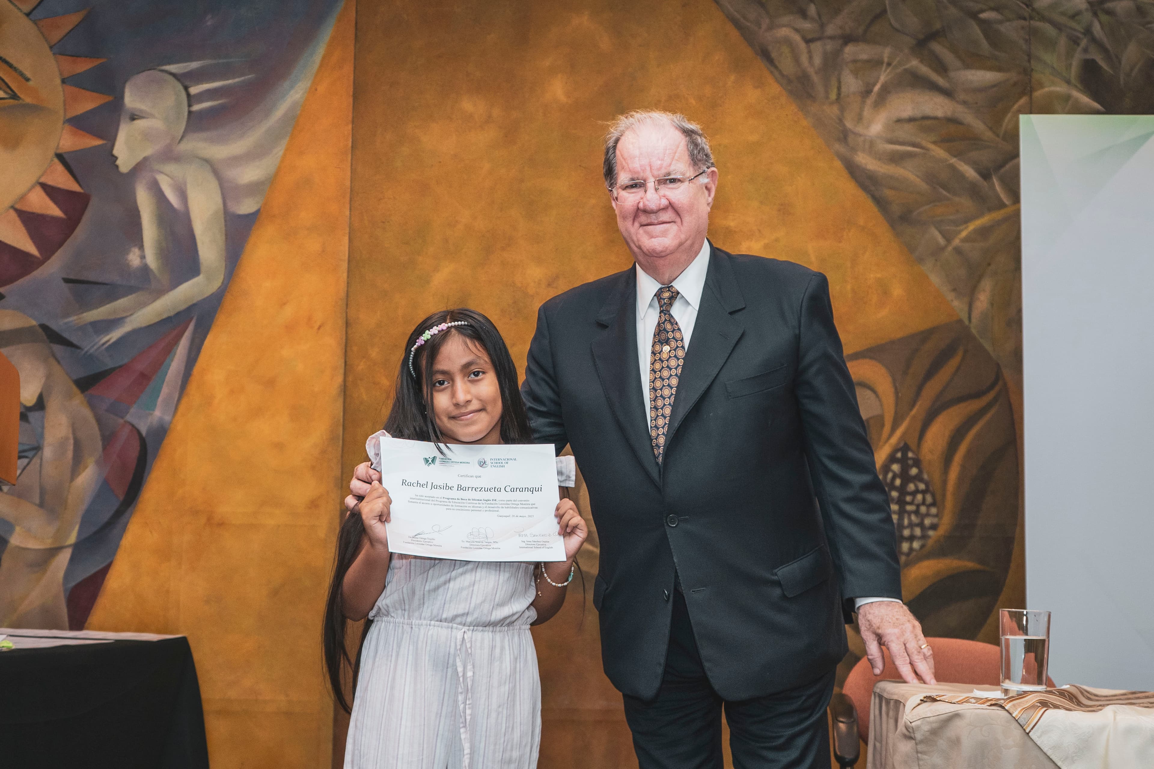 Becaria recibiendo su certificado junto a directivos de FLOM